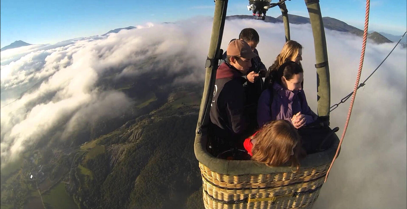 Pasajeros en la cesta de un globo volando sobre un mar de niebla